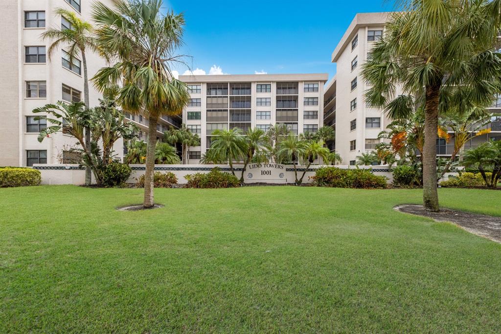 A grassy lawn sits in front of the Lido Towers apartment building with palm trees — 1001 BENJAMIN FRANKLIN DRIVE UNIT 512, SARASOTA, FL