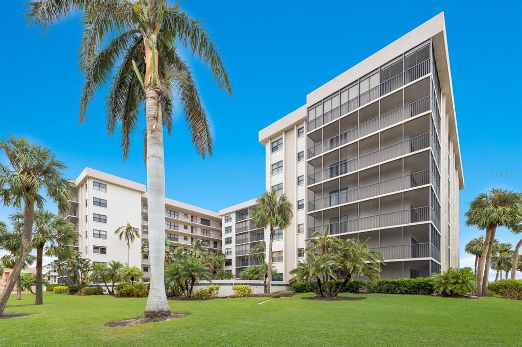 A multi-story apartment building with screened balconies stands on a grassy lawn with palm trees — 1001 BENJAMIN FRANKLIN DRIVE UNIT 512, SARASOTA, FL