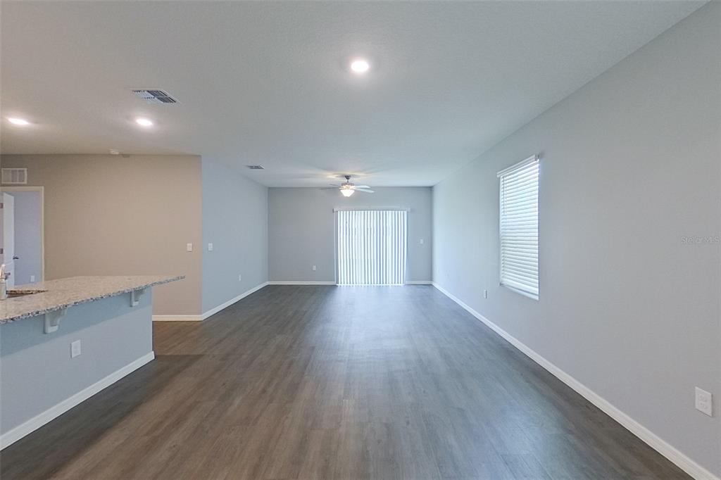 An open-concept living area features gray walls, wood-look flooring, a ceiling fan, and sliding doors — 32217 EDSON AVENUE, LEESBURG, FL