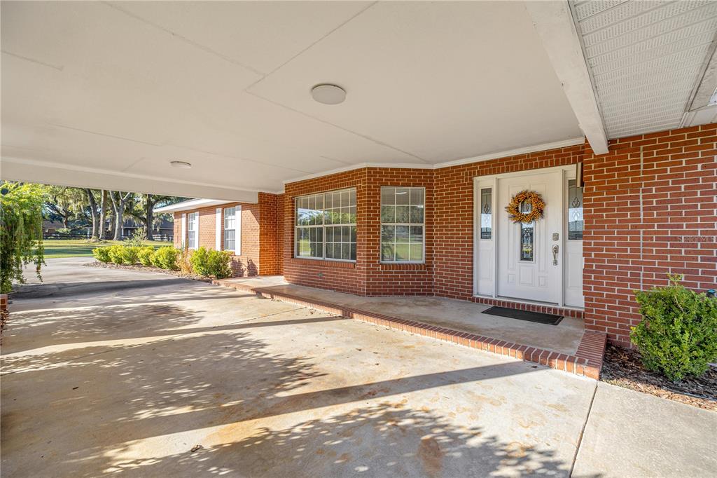 A brick house exterior features a covered carport and a white front door with a wreath — 9812 SW 74TH AVENUE, OCALA, FL