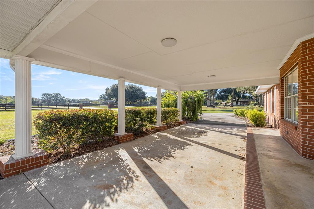 A covered concrete patio features white columns and brick bases overlooking a grassy yard — 9812 SW 74TH AVENUE, OCALA, FL