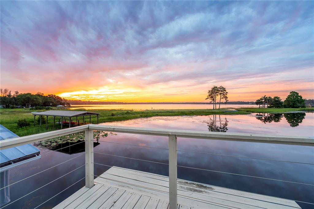 A wooden deck overlooks a calm lake and a boat dock at sunset — 4931 DORA DRIVE, MOUNT DORA, FL