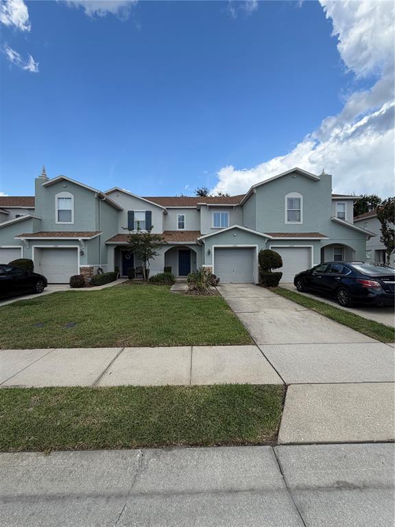 A row of multi-story townhouses features light blue siding, attached garages, and concrete driveways — 2573 AVENTURINE STREET, KISSIMMEE, FL