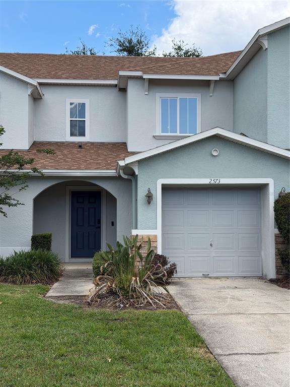 A two-story townhouse features a blue front door, a single-car garage, and light-colored stucco — 2573 AVENTURINE STREET, KISSIMMEE, FL