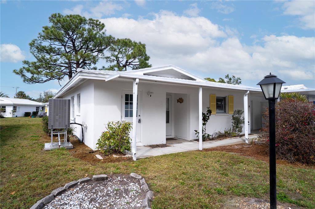 A white single-story house with a covered porch, yellow shutters, and a large pine tree — 216 FAIR WINDS DRIVE UNIT 216, NOKOMIS, FL