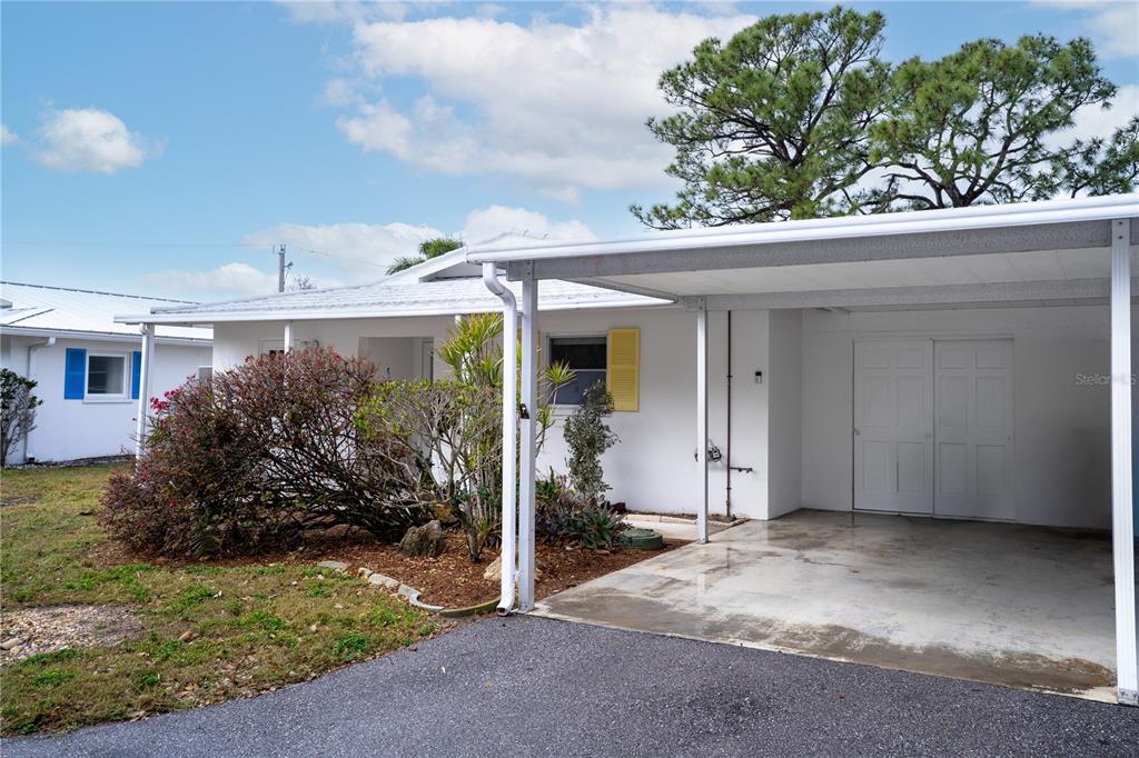 A white single-story house features a front carport, a paved driveway, and a landscaped yard — 216 FAIR WINDS DRIVE UNIT 216, NOKOMIS, FL