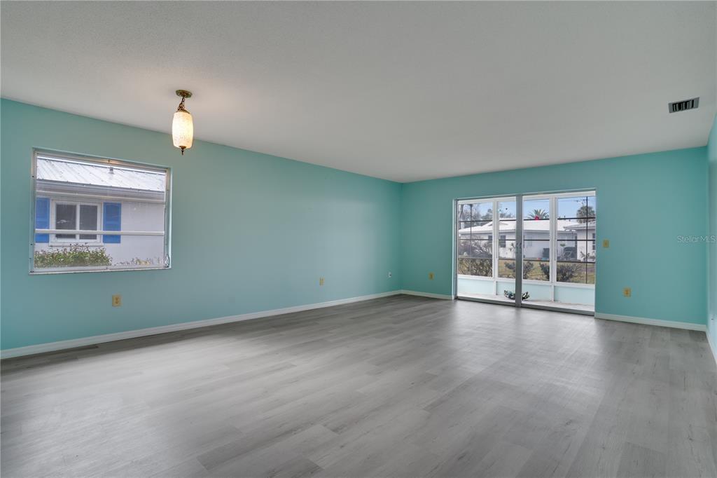 An empty room with light blue walls, gray wood-look flooring, and a sliding glass door — 216 FAIR WINDS DRIVE UNIT 216, NOKOMIS, FL