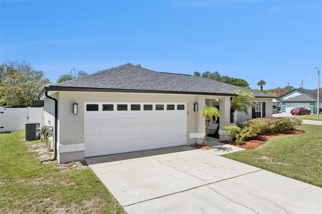 A single-story house with a white garage door, concrete driveway, and a gray shingled roof — 14004 AMES AVENUE, ORLANDO, FL