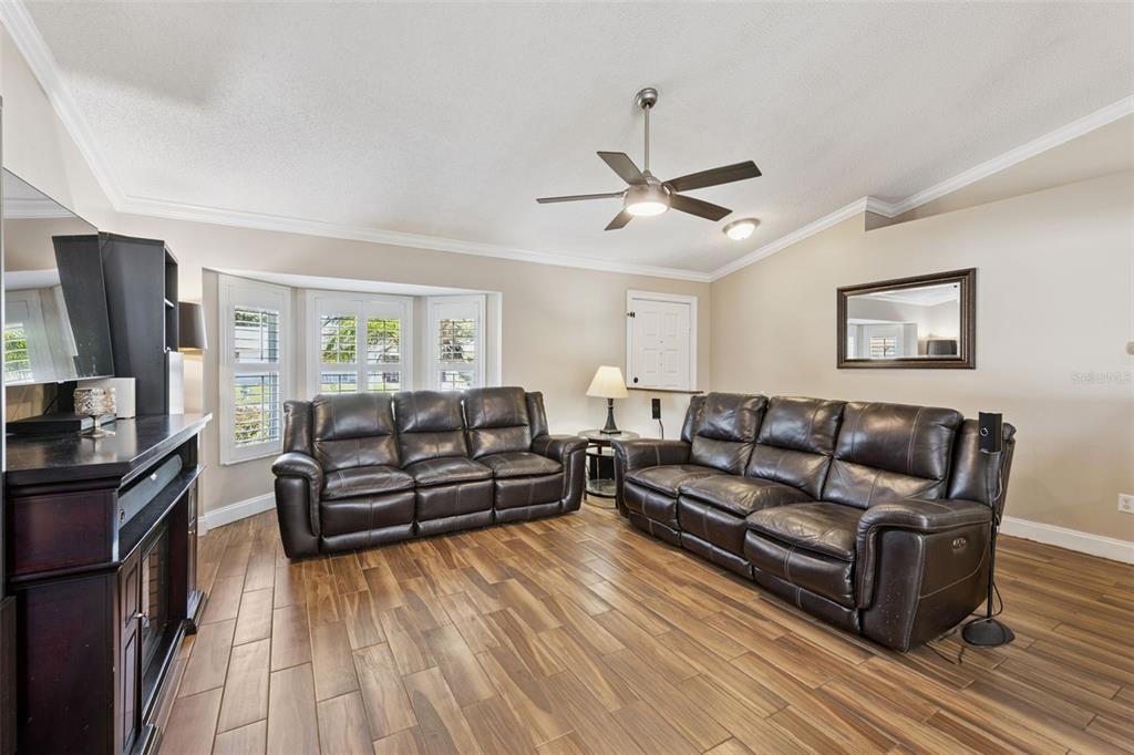 A living room features two dark leather sofas, wood-look tile flooring, and a ceiling fan — 14004 AMES AVENUE, ORLANDO, FL