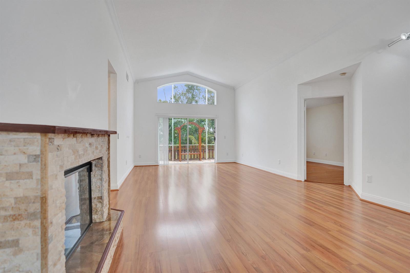 A spacious living room features a stone fireplace, vaulted ceilings, and sliding glass doors — 6817 Barnwell Drive, Boynton Beach FL 33437, BOYNTON BEACH, FL