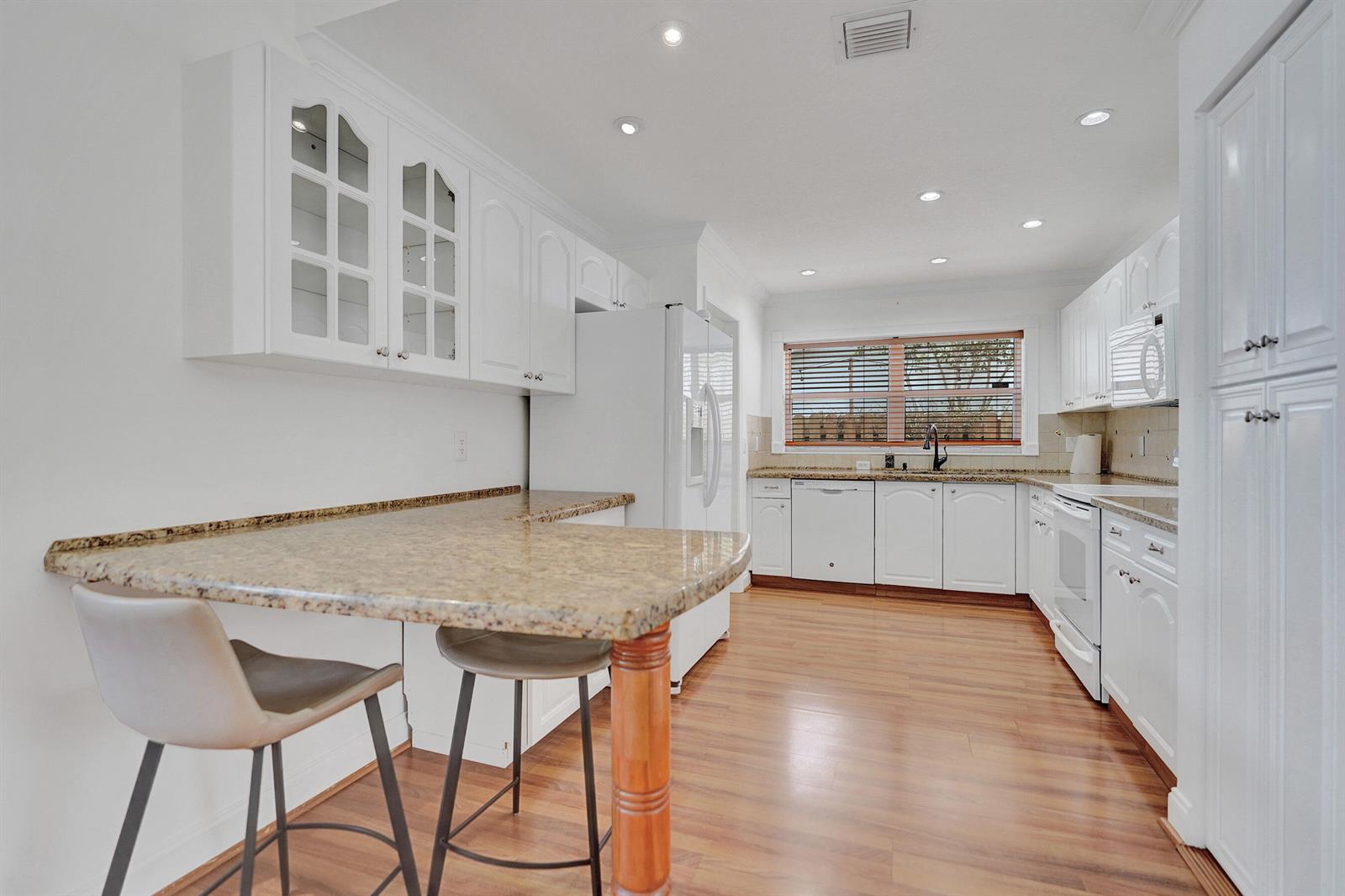 A kitchen features white cabinets, granite countertops, a breakfast bar, and wood-look flooring — 6817 Barnwell Drive, Boynton Beach FL 33437, BOYNTON BEACH, FL