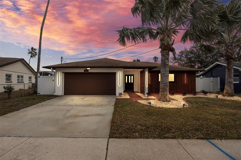 A single-story house with a brown garage door, wood-slat siding, and palm trees at sunset — 5921 DENVER STREET NE, ST PETERSBURG, FL