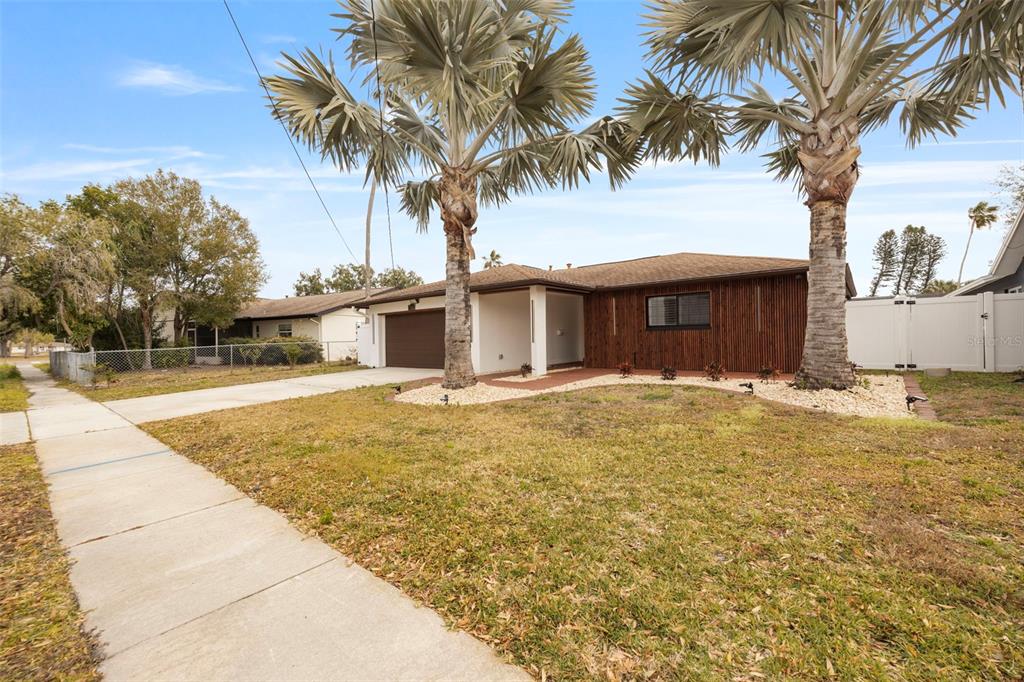 A single-story house with a brown garage, vertical wood siding, and two palm trees — 5921 DENVER STREET NE, ST PETERSBURG, FL