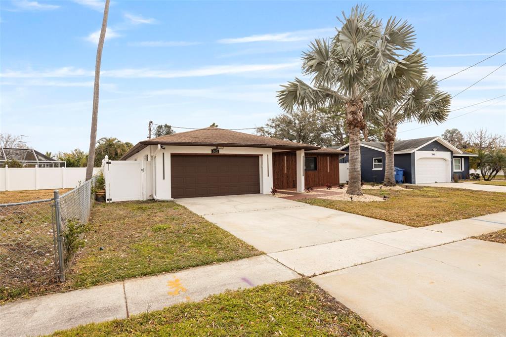 A single-story house with a brown garage door, white exterior, and a large palm tree — 5921 DENVER STREET NE, ST PETERSBURG, FL