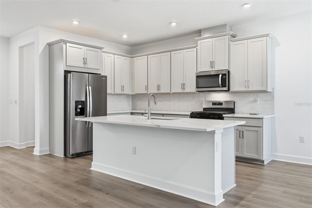 A modern kitchen features light gray cabinets, stainless steel appliances, and a white quartz island — 1895 SEAWALL WAY, CELEBRATION, FL