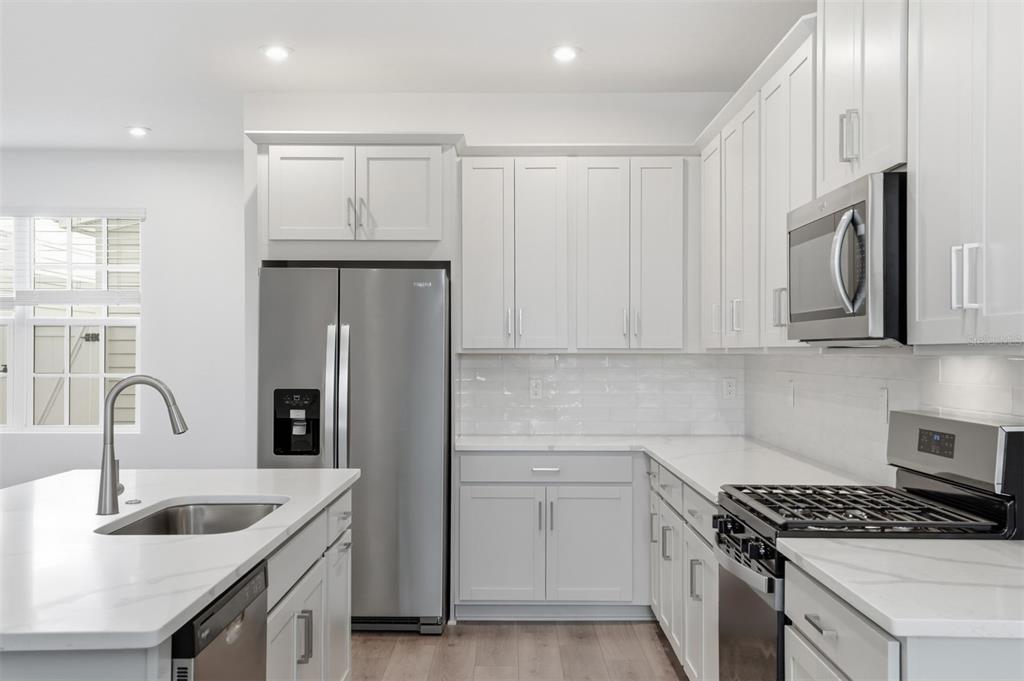A modern kitchen features white cabinets, stainless steel appliances, and a marble-topped island — 1895 SEAWALL WAY, CELEBRATION, FL