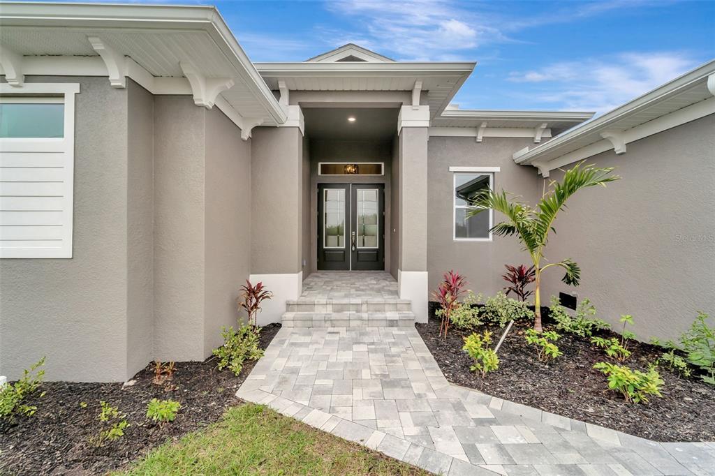 A paved walkway leads to the double front doors of a gray stucco house — 10442 WINNIPEG STREET, PORT CHARLOTTE, FL