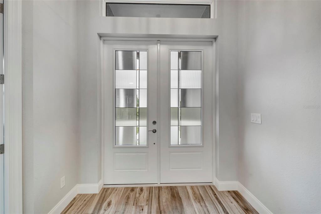 A white double front door with glass panels sits in a room with light flooring — 10442 WINNIPEG STREET, PORT CHARLOTTE, FL