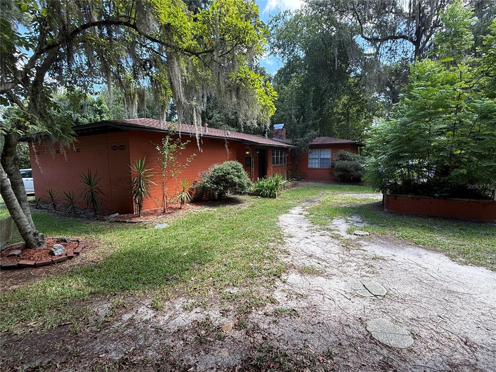 A single-story orange brick house with a dirt driveway sits among trees and landscaping — 1830 SW WILLISTON ROAD, GAINESVILLE, FL