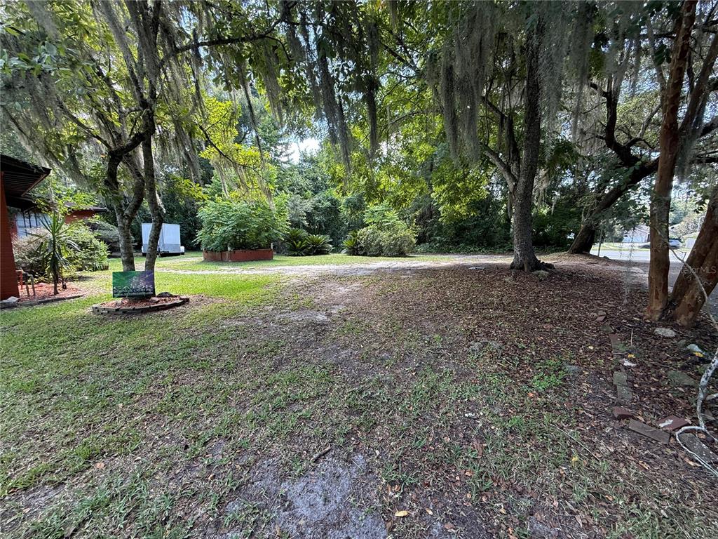 A grassy, tree-shaded yard with a small sign and a trailer in the background — 1830 SW WILLISTON ROAD, GAINESVILLE, FL