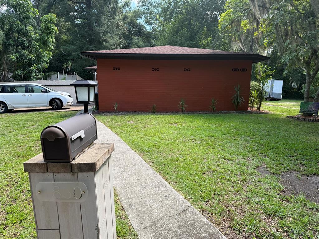 A mailbox stands in the foreground of a lawn leading to a red, single-story building — 1830 SW WILLISTON ROAD, GAINESVILLE, FL