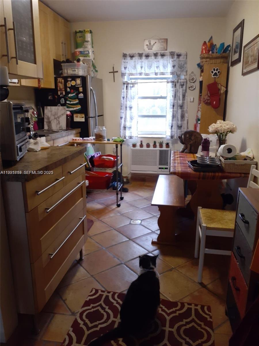 A kitchen with light wood cabinets, tile flooring, a dining table, and two cats — 645 NE 77th St # 8, Miami FL 33138, MIAMI, FL