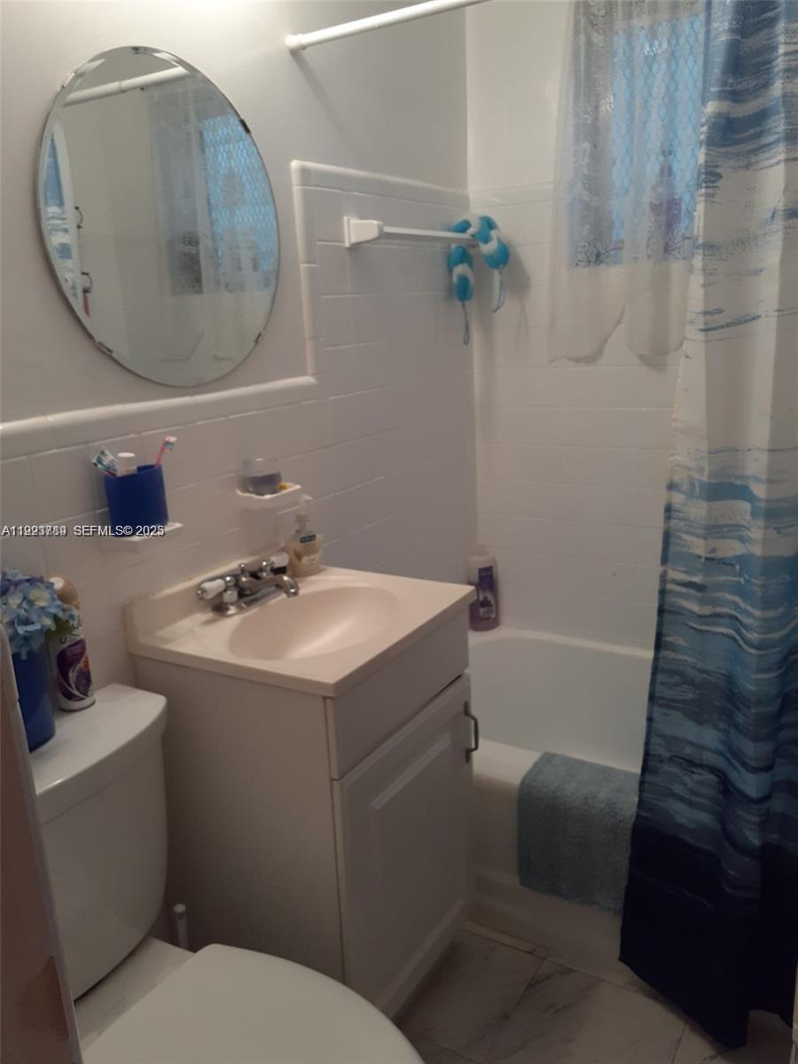 A small bathroom features a white vanity, oval mirror, and a shower-tub combination — 645 NE 77th St # 8, Miami FL 33138, MIAMI, FL