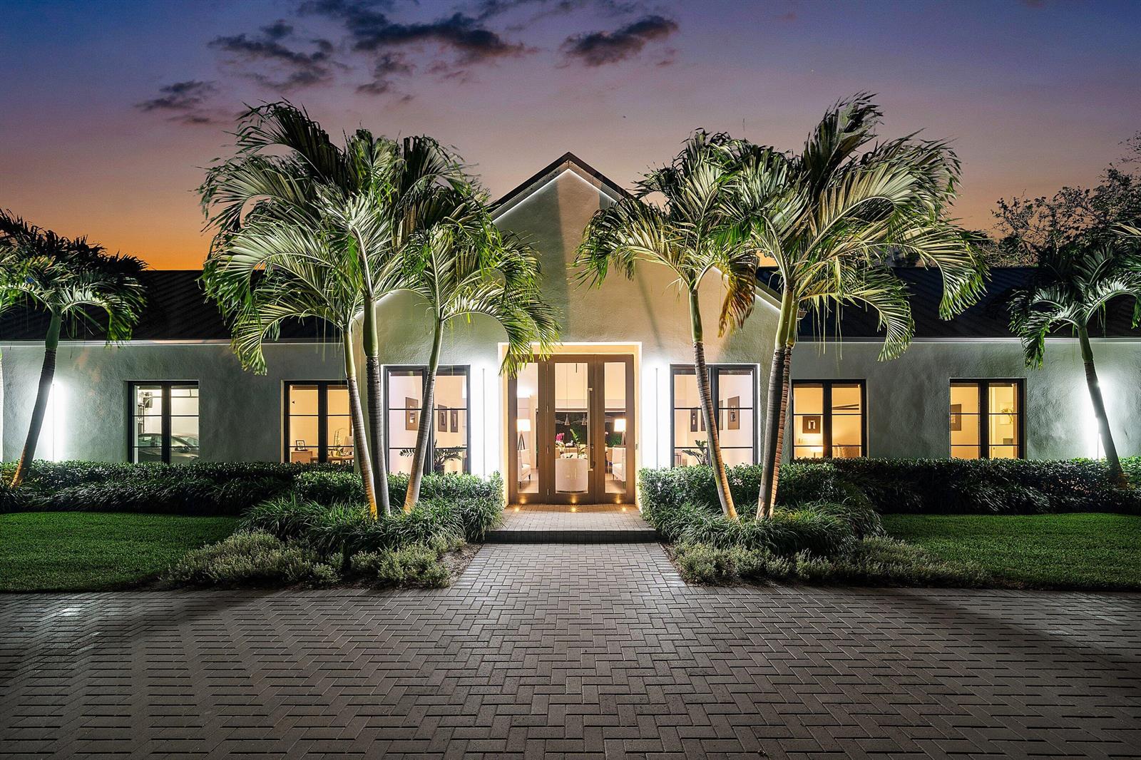 A single-story house with a brick driveway, palm trees, and illuminated windows at dusk — 1275 N Swinton Avenue, Delray Beach FL 33444, DELRAY BEACH, FL