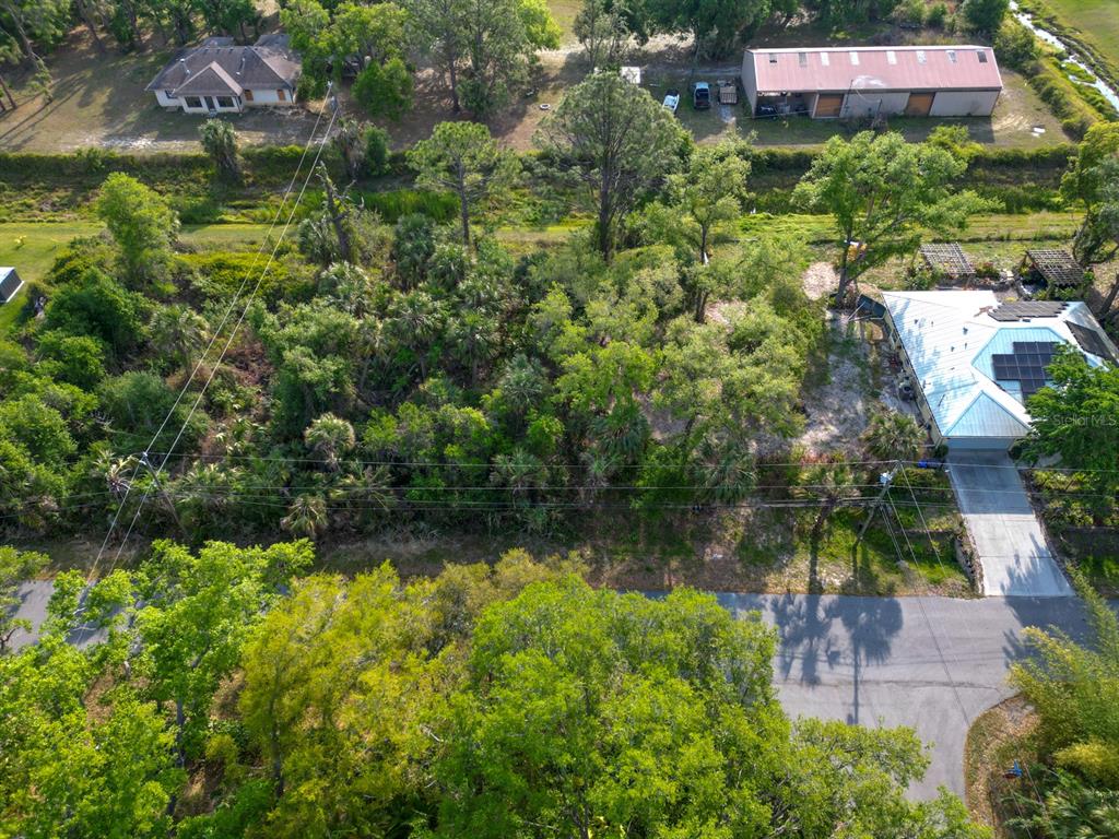 An aerial view shows a wooded lot situated between a residential house and a metal building — GALAMBOS STREET, NORTH PORT, FL