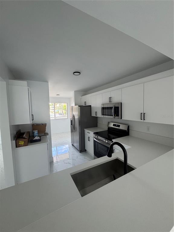 A modern kitchen features white cabinets, stainless steel appliances, and light-colored tile flooring — 7751 SOUTHAMPTON TERRACE UNIT 213, TAMARAC, FL