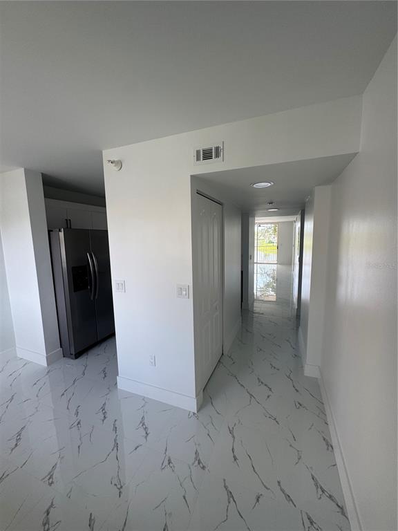A hallway with white marble-patterned tile floors leads toward a glass door overlooking water — 7751 SOUTHAMPTON TERRACE UNIT 213, TAMARAC, FL