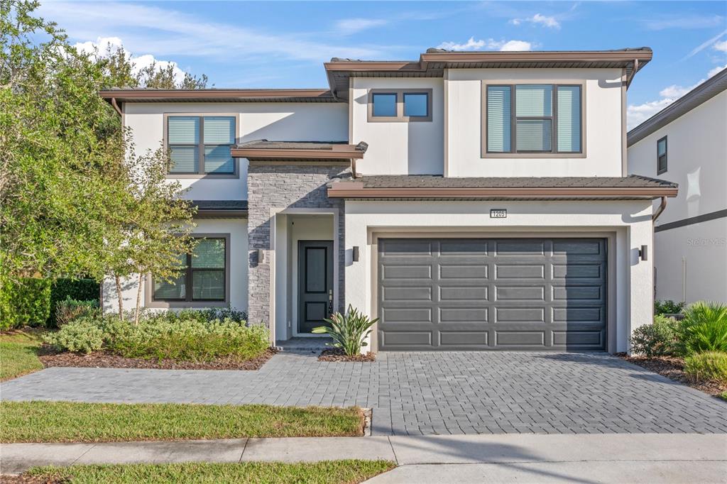 A two-story house with a stone-accented entryway, a two-car garage, and a paved driveway — 1205 BUTTERFLY ORCHID ROAD, DAVENPORT, FL
