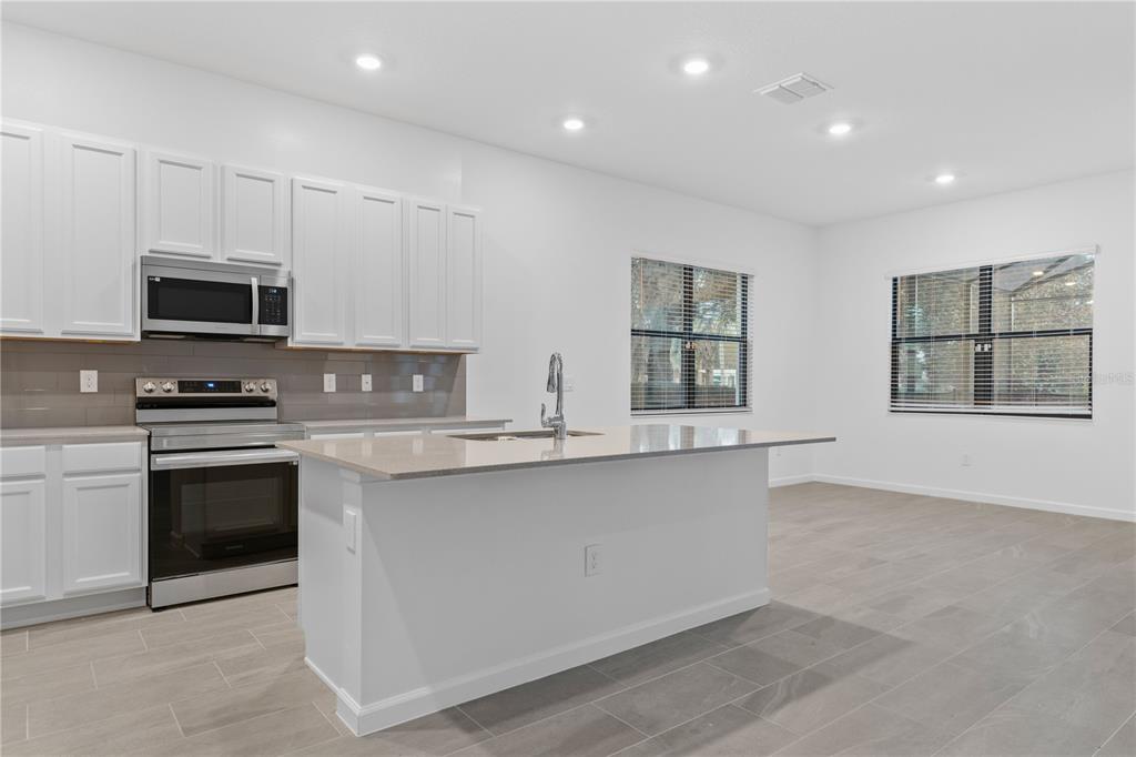 A modern kitchen features white cabinets, stainless steel appliances, a center island, and tile flooring — 1205 BUTTERFLY ORCHID ROAD, DAVENPORT, FL