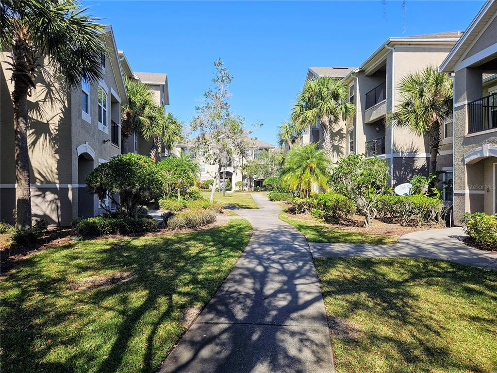 A concrete walkway leads between two multi-story apartment buildings surrounded by palm trees and landscaping — 6548 SWISSCO DRIVE UNIT 628, ORLANDO, FL