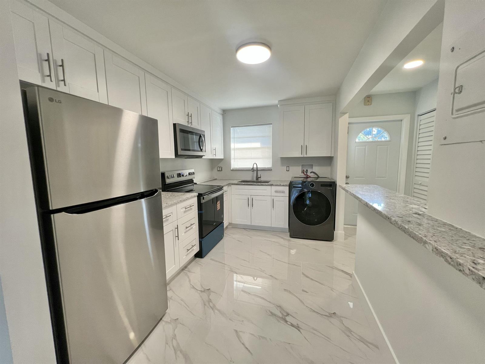 A kitchen with white cabinets, stainless steel appliances, a washer, and marble-patterned tile flooring — 601 S State Road 7 # 2c, Margate FL 33068, MARGATE, FL