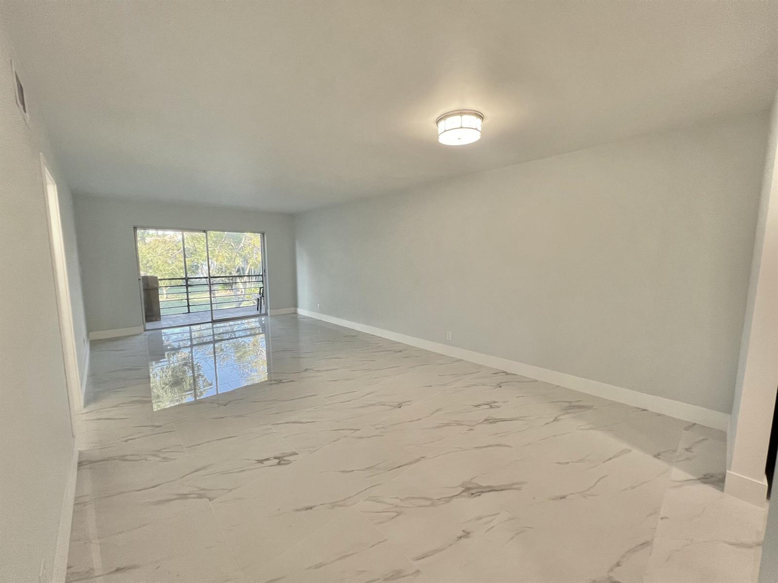 An empty living room features white marble-look tile flooring, light gray walls, and a sliding glass door — 601 S State Road 7 # 2c, Margate FL 33068, MARGATE, FL
