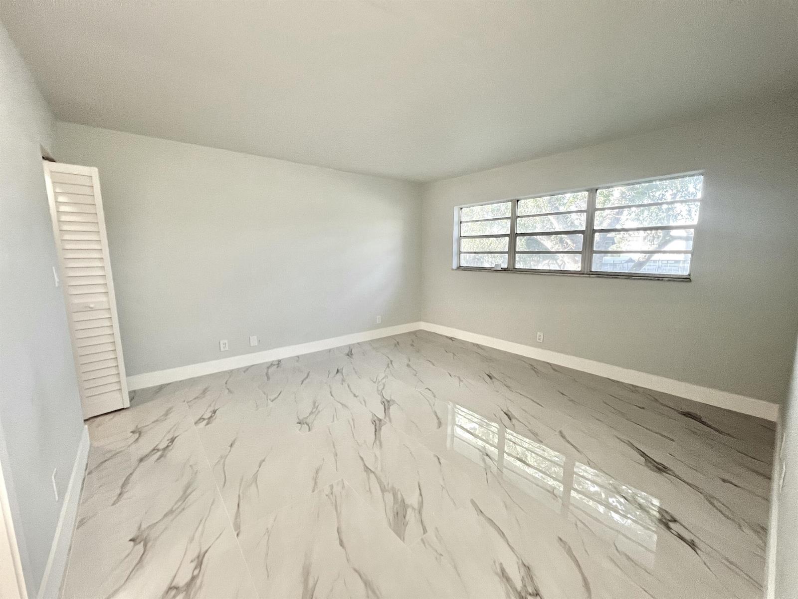 An empty room features light gray walls, white baseboards, and polished white marble-patterned tile flooring — 601 S State Road 7 # 2c, Margate FL 33068, MARGATE, FL