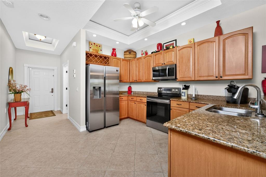 A kitchen with light wood cabinets, granite countertops, stainless steel appliances, and a ceiling fan — 3228 WOOD THRUSH DRIVE UNIT 112, PUNTA GORDA, FL