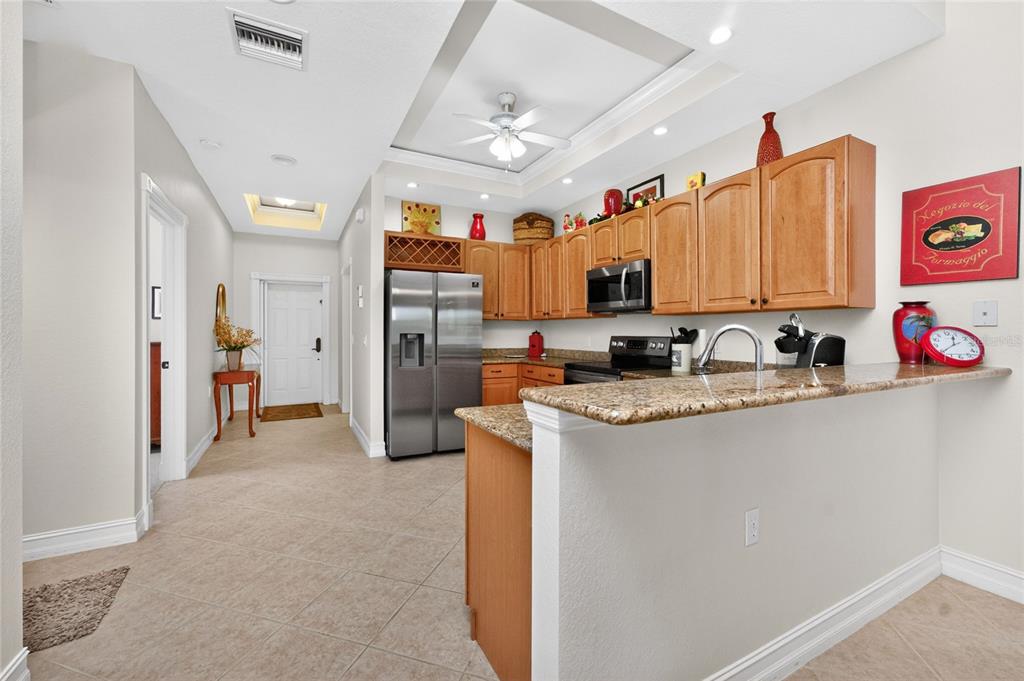 A kitchen with wood cabinets, granite countertops, and stainless steel appliances opens to a hallway — 3228 WOOD THRUSH DRIVE UNIT 112, PUNTA GORDA, FL