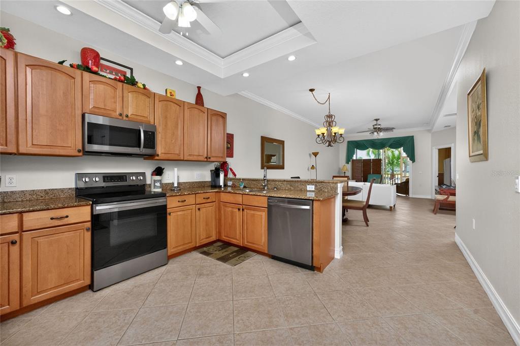 A kitchen with wood cabinets, granite countertops, and stainless steel appliances opens to a dining area — 3228 WOOD THRUSH DRIVE UNIT 112, PUNTA GORDA, FL