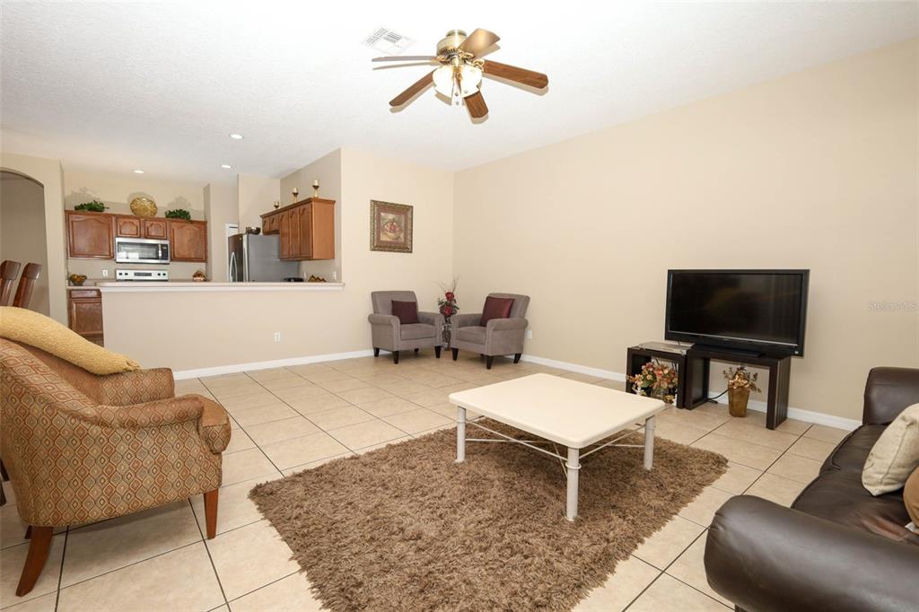 A living room with tile floors, a brown area rug, and an open kitchen view — 426 ALEXANDRIA PLACE DRIVE, APOPKA, FL