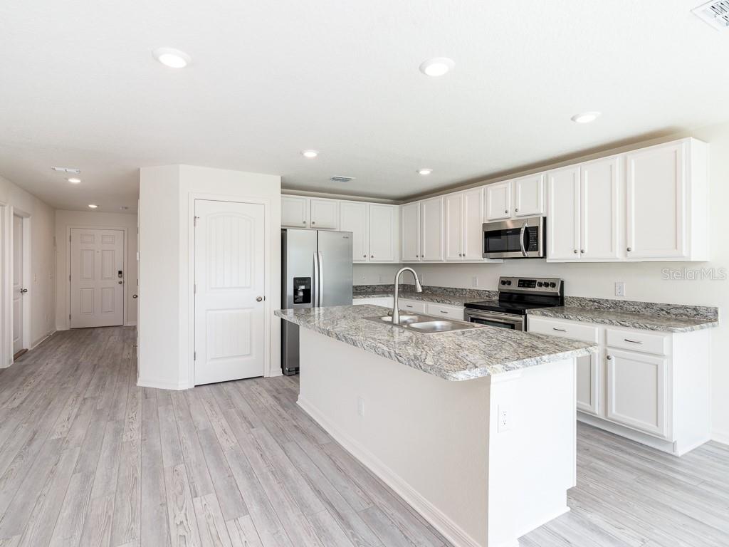 A kitchen features white cabinets, granite countertops, a center island, and light wood-look flooring — 1359 HAGERICK LANE, NORTH PORT, FL