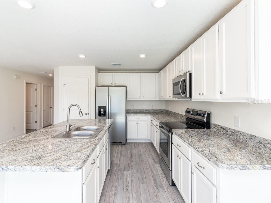 A kitchen with white cabinets, granite countertops, stainless steel appliances, and wood-look flooring — 1359 HAGERICK LANE, NORTH PORT, FL