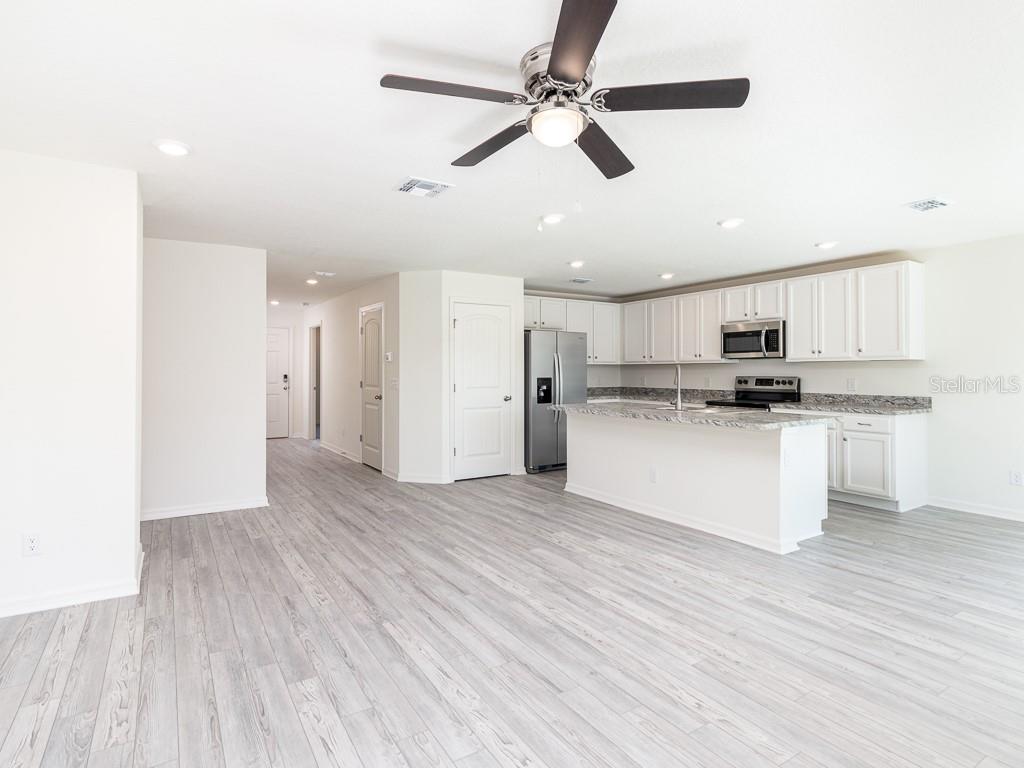An open-concept kitchen and living area featuring white cabinets, granite countertops, and light-colored flooring — 1359 HAGERICK LANE, NORTH PORT, FL