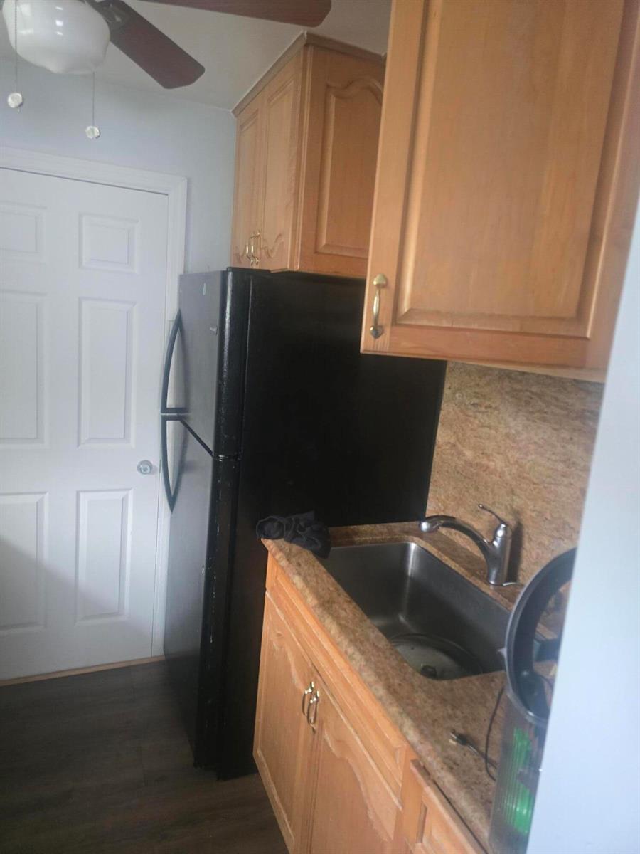A small kitchen features light wood cabinets, a black refrigerator, and a stainless steel sink — 3016 E Palm Drive, Boynton Beach FL 33435, BOYNTON BEACH, FL