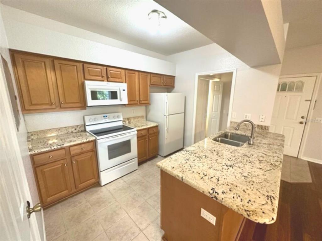 A kitchen features wood cabinets, granite countertops, white appliances, and a central island with sink — 903 EAGLE POND DRIVE UNIT 903, WINTER HAVEN, FL