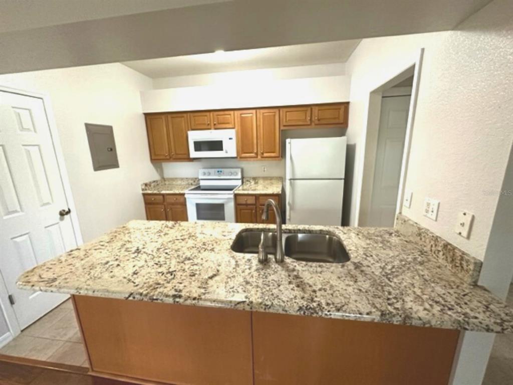 A kitchen features wood cabinets, granite countertops, a stainless steel sink, and white appliances — 903 EAGLE POND DRIVE UNIT 903, WINTER HAVEN, FL