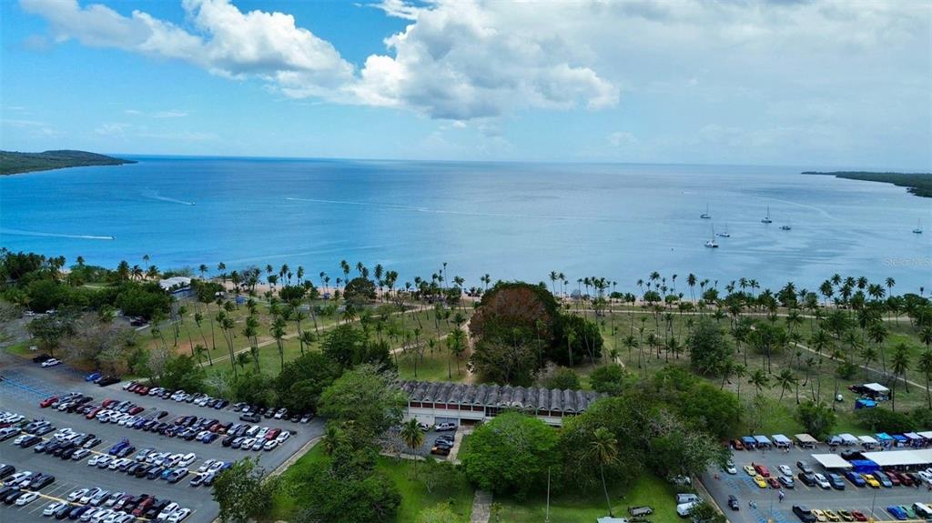 An aerial view shows a parking lot, a long building, palm trees, and the ocean — Sola 10 BO LLANOS COSTA, BOQUERON, PR