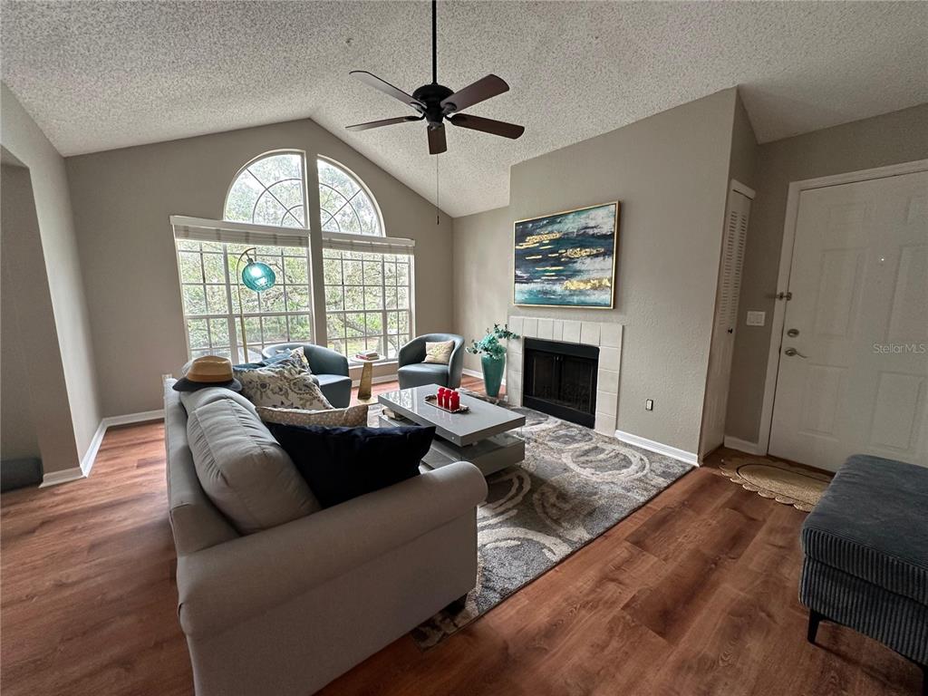 A living room features a vaulted ceiling, fireplace, large arched windows, and wood-look flooring — 995 NORTHERN DANCER WAY UNIT 201, CASSELBERRY, FL