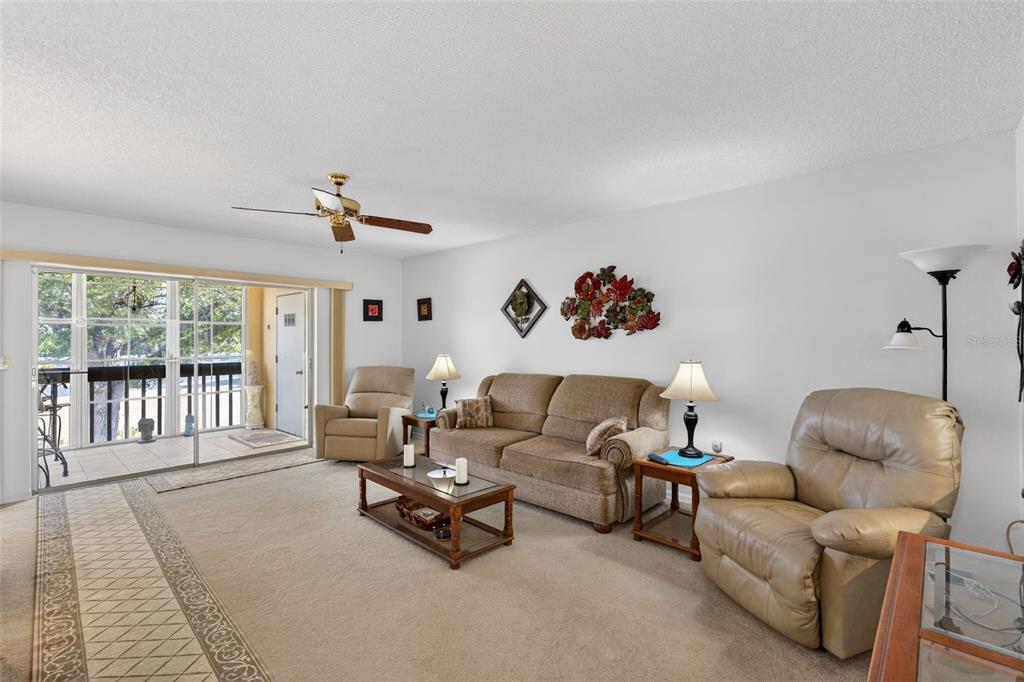 A living room features beige carpet, a tan sofa, two recliners, and a ceiling fan — 6699 SAN CASA DRIVE UNIT L8, ENGLEWOOD, FL
